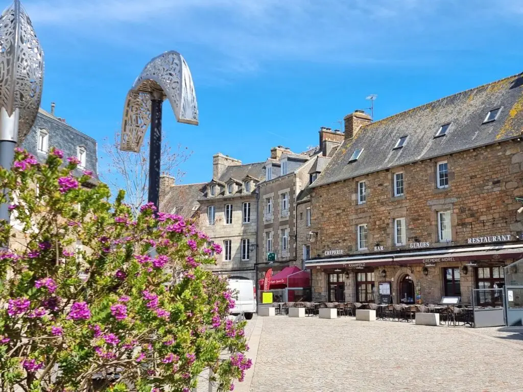 Frankreich im Juni: Sonniger Platz in Paimpol in der Bretagne mit blühenden Blumen, historischen Steinhäusern und Straßencafés.